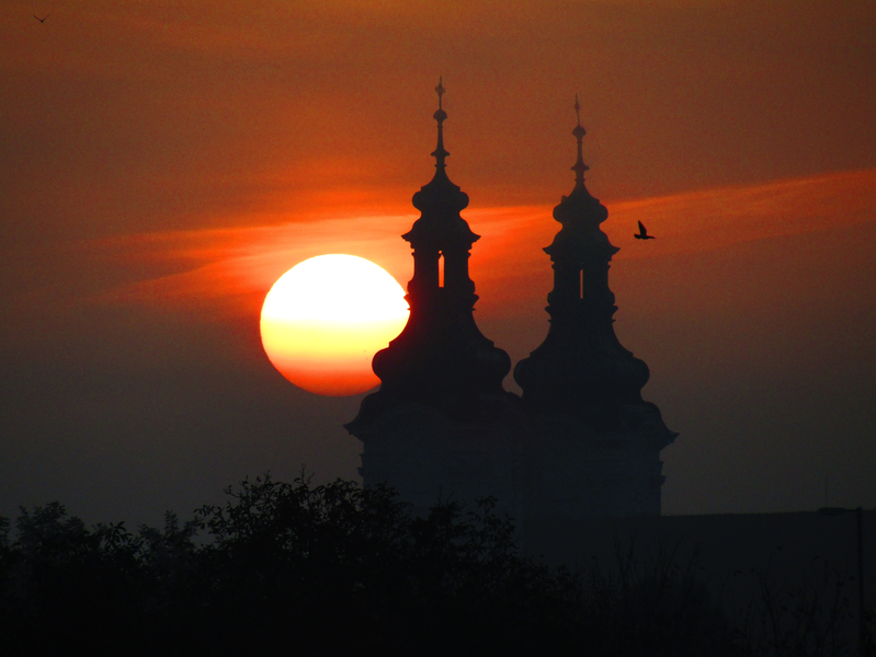 vycházející slunce a silueta Hradištského kostela s letícím holubem